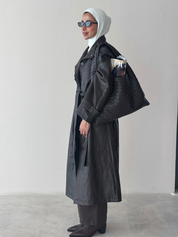 Person wearing a long dark coat and sunglasses on a plain background